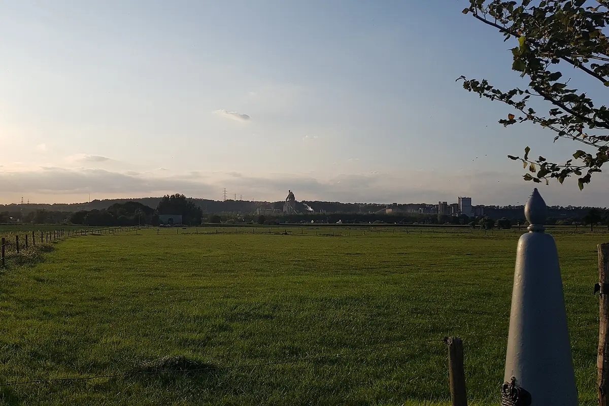 Een witte grenspaal aan de rand van een weiland bij zonsondergang